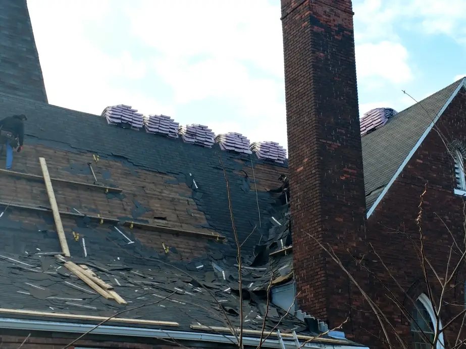 Stripped roof deck beside a tall brick chimney on the church